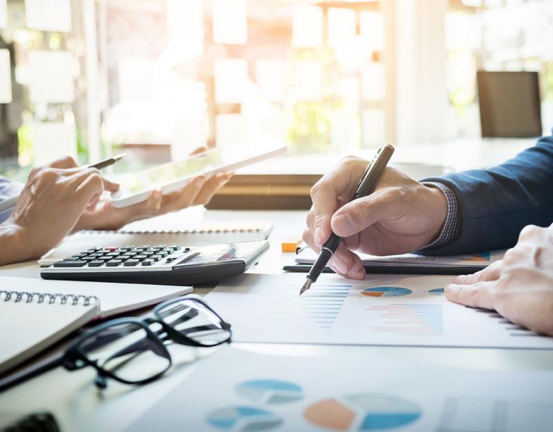 Two pairs of hands holding pens, leaning on a table with charts and office supplies