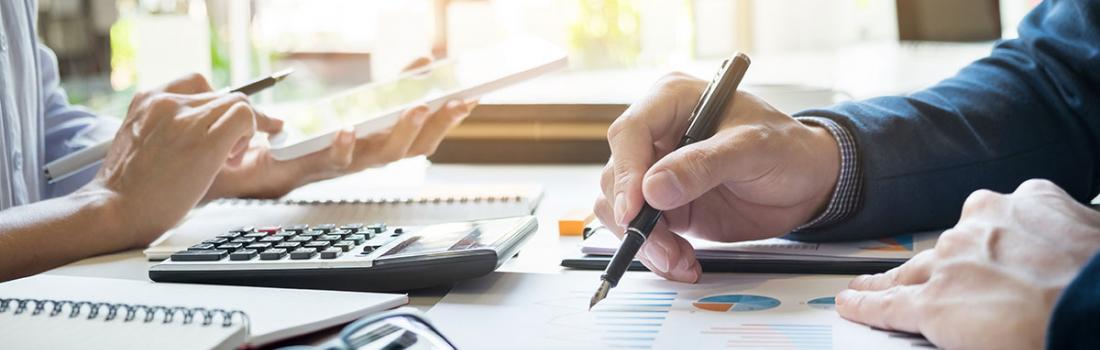 Two pairs of hands holding pens, leaning on a table with charts and office supplies